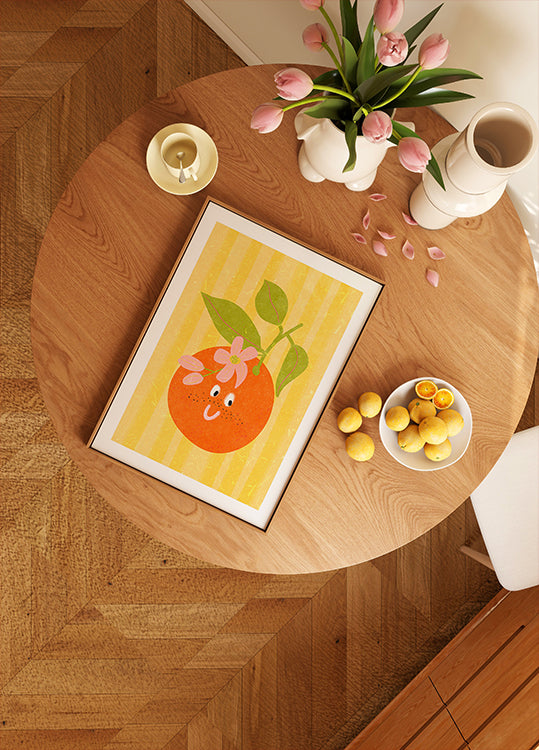 dřevěný stůl se zarámovaným obrázkem pomeranče, miska citronů, váza s růžovými tulipány a svíčka na něm.